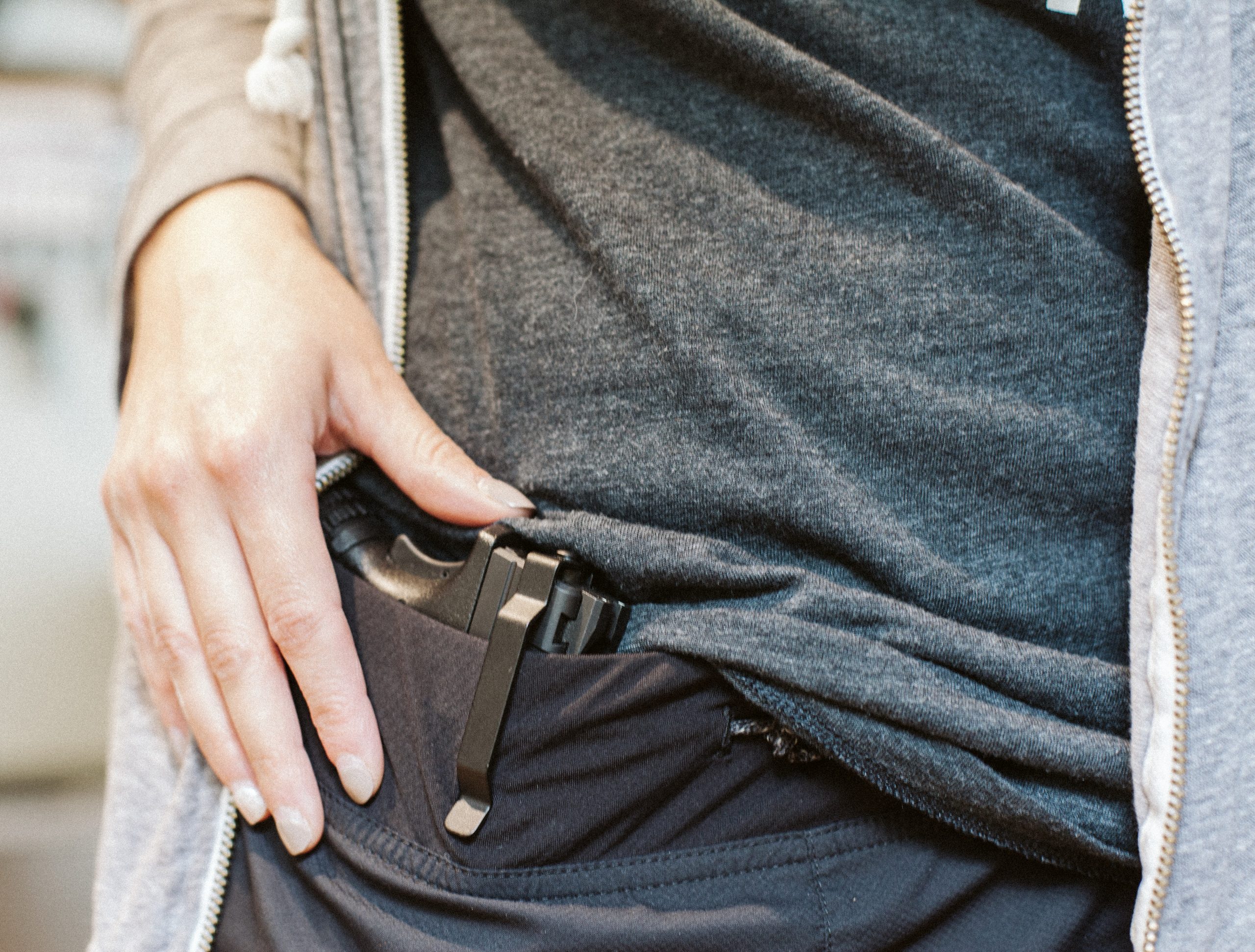 Close-up image of a person wearing casual clothing, lifting their shirt slightly to reveal a concealed handgun secured with a Clipdraw gun clip inside the waistband.