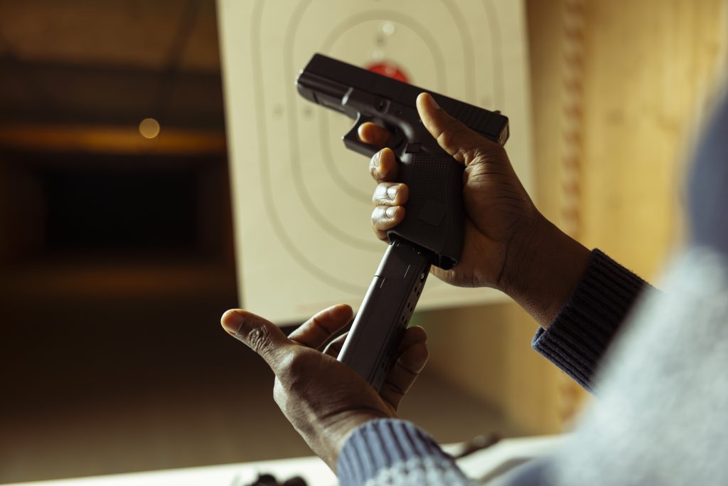 Close-up of a person reloading a handgun magazine at an indoor shooting range with a target in the background.